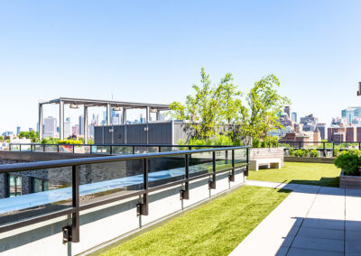 Spacious rooftop green area with cabana, plants, and a city view of Brooklyn.