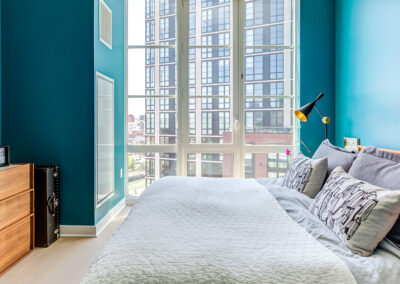 Furnished bedroom on hardwood floors with blue walls and large windows for a beautiful city view.