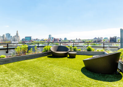 Rooftop lounge on faux grass with chairs and flowers surrounding the area.