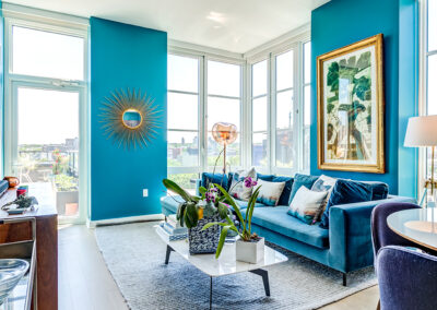 Furnished living room on hardwood floors with blue walls, blue couch, and large windows with city views.