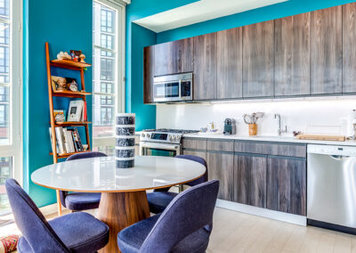 Gowanus apartments furnished kitchen area with wooden cupboards, blue walls, and a small circular dining table.